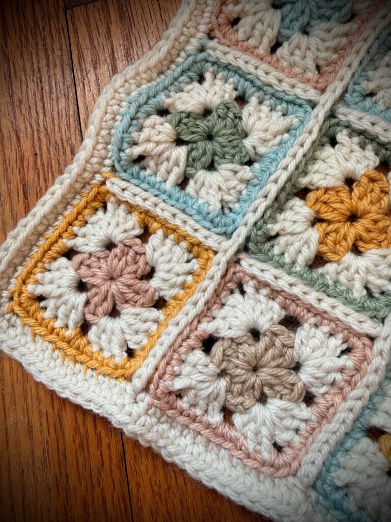 Close-up of a crochet granny square blanket showing a double row of single crochet border in cream around soft pastel squares.