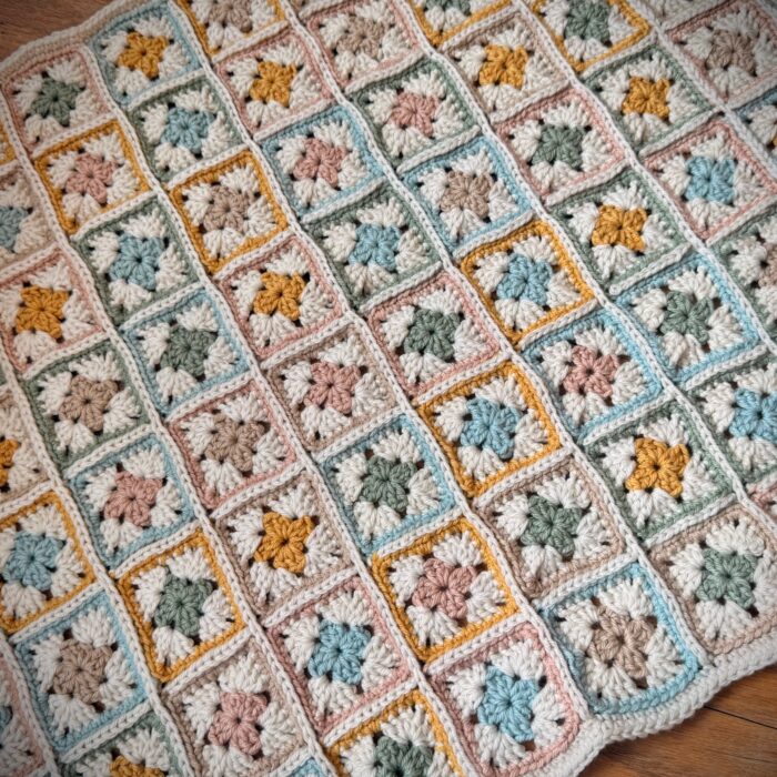 Finished crochet granny square blanket in soft pastel colors with cream joining and border, laid flat to show full layout and texture.